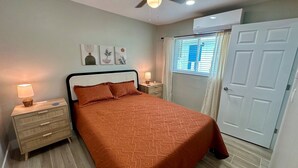A bedroom with a bed, nightstands, a window with curtains, and a door. - Turtle Nest 4 - Quick Walk to Beach (Fort Myers Beach)