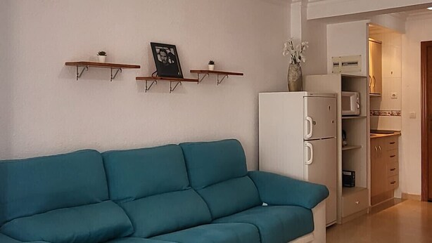 A living room with a teal sectional sofa, a white refrigerator, and a ceiling fan. - TERRASOL PLAZAMAR 4-2 (Torre del Mar)