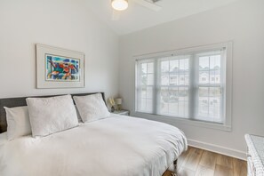 Une chambre à coucher avec un grand lit, un tableau encadré, une table de chevet et une fenêtre avec des stores.