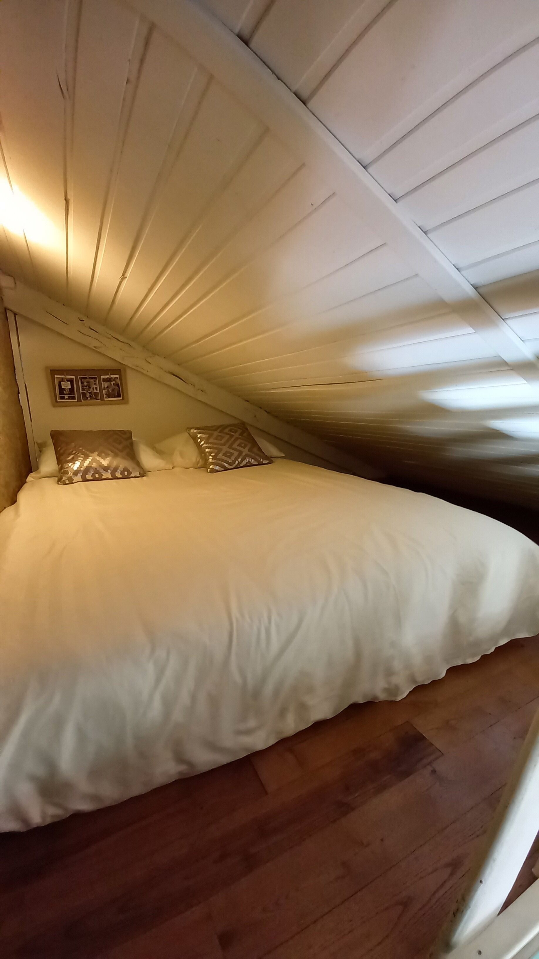 Un dormitorio con piso de madera, una cama con ropa blanca y techo inclinado.