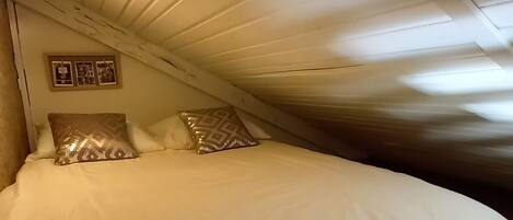 Un dormitorio con piso de madera, una cama con ropa blanca y techo inclinado.