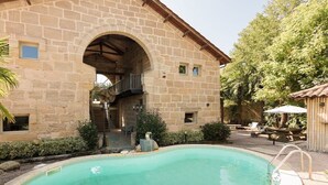 Um edifício de pedra com piscina, área de estar ao ar livre e espaço coberto.