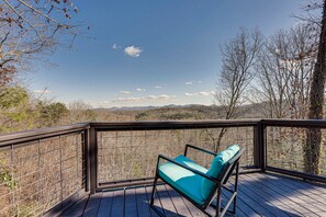 A wooden deck with a metal railing, a single blue cushioned chair, and a view of a mountainous landscape.