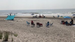 Une plage avec plusieurs parasols et chaises de couleur bleue, dont certains abritent des personnes.