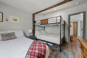 Une chambre avec un lit superposé, un bureau, une table de chevet, une couverture à carreaux et une porte donnant sur une salle de bain.