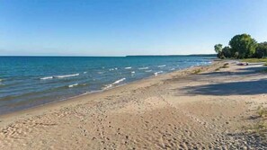 Une plage avec un ciel dégagé, une eau calme et une ligne d’arbres à l’horizon.