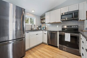 A modern kitchen with stainless steel appliances, white cabinets, and a wooden floor.