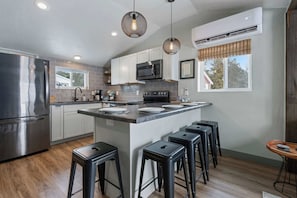 A modern kitchen with a central island, bar stools, stainless steel appliances, and pendant lighting.