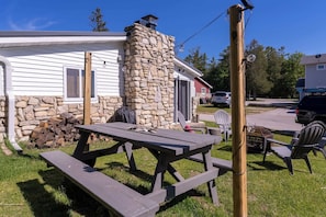 A wooden picnic table with benches, a stone chimney, and a white house with a garage. - Little White Cottage Lake Michigan sandy beach (Sturgeon Bay)