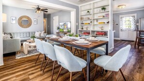 Un coin repas avec une table en bois, des chaises bleu clair et une étagère blanche contenant divers objets.