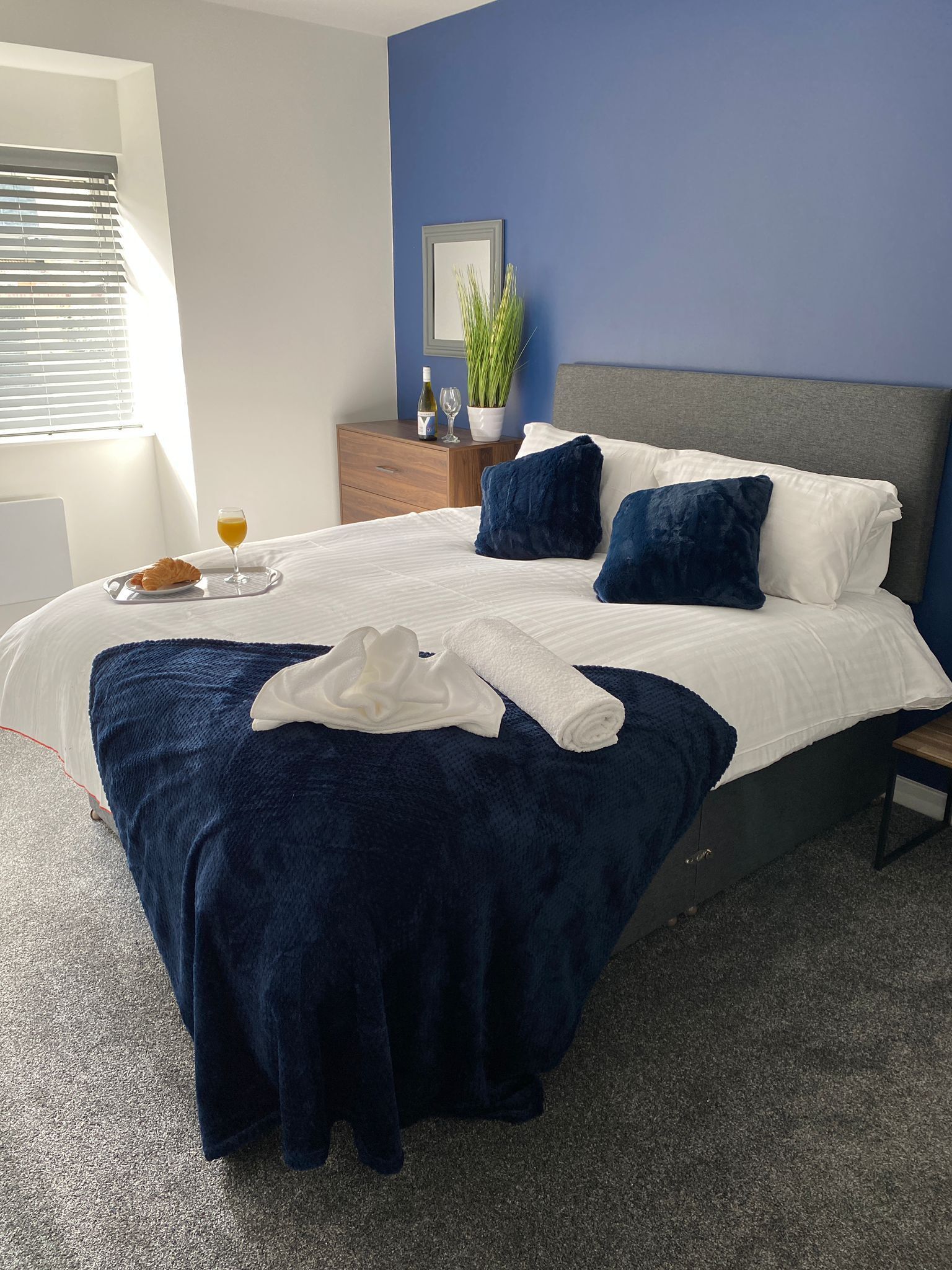Un letto rifatto con copriletto bianco, cuscini blu scuro e una coperta azzurra, con un accappatoio bianco sul letto.