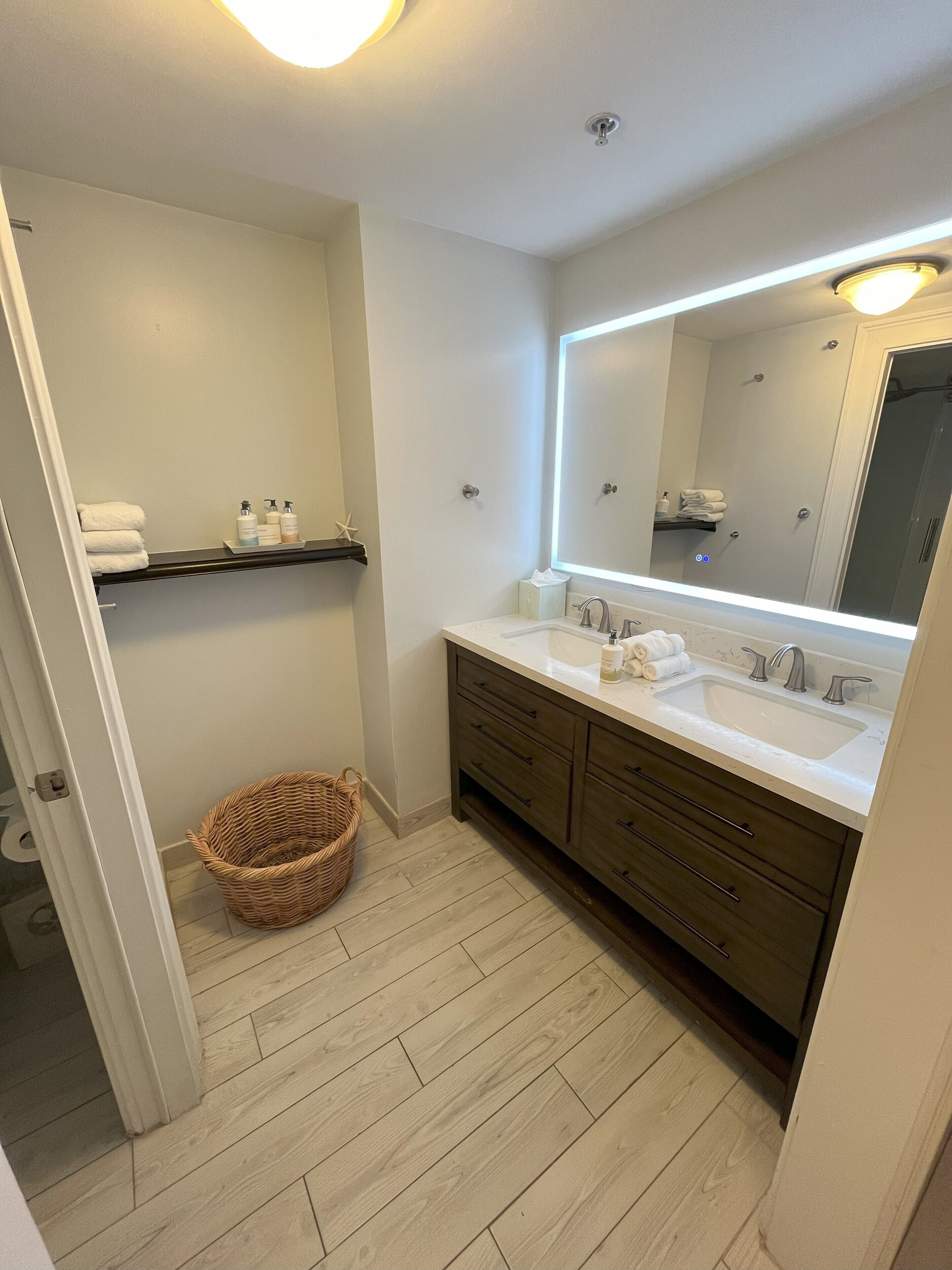 Un baño con dos lavamanos, un espejo grande y una cesta de mimbre en el suelo.