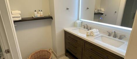 Un baño con dos lavamanos, un espejo grande y una cesta de mimbre en el suelo.