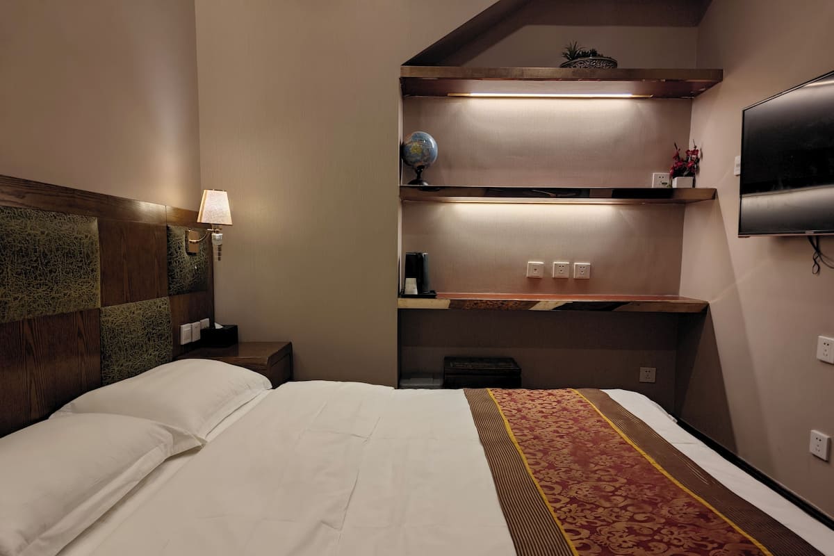 Une chambre d’hôtel comprenant un lit, une table de chevet, une lampe, une étagère avec un globe terrestre et un téléviseur fixé au mur.