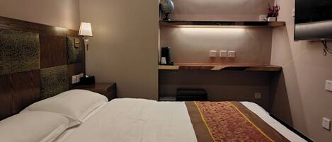 Una habitación de hotel con una cama, una mesita de noche, una lámpara, una estantería con un globo terráqueo y un televisor montado en la pared.