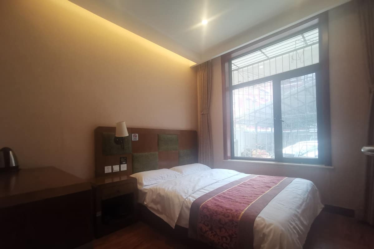 Une chambre d’hôtel équipée d’un lit, d’une table de chevet, d’une lampe et d’une fenêtre donnant sur l’extérieur.