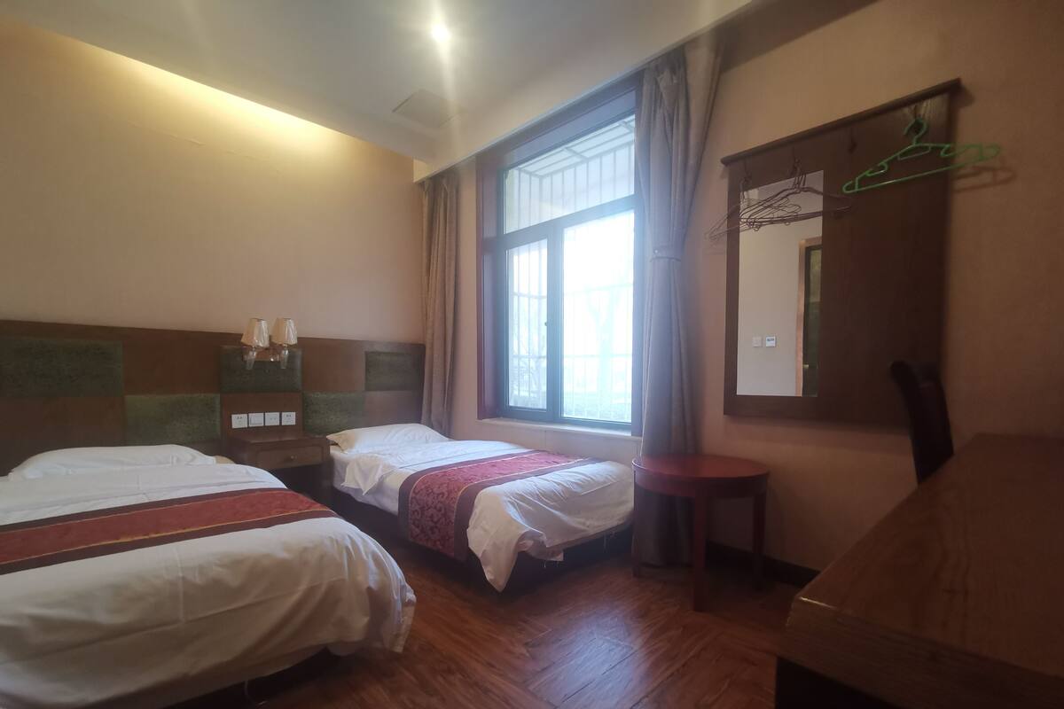 Une chambre d’hôtel avec deux lits, un petit bureau, un miroir et une fenêtre avec des rideaux.