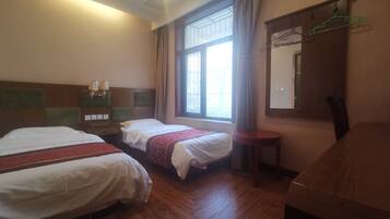 Una habitación de hotel con dos camas, un escritorio pequeño, un espejo y una ventana con cortinas.