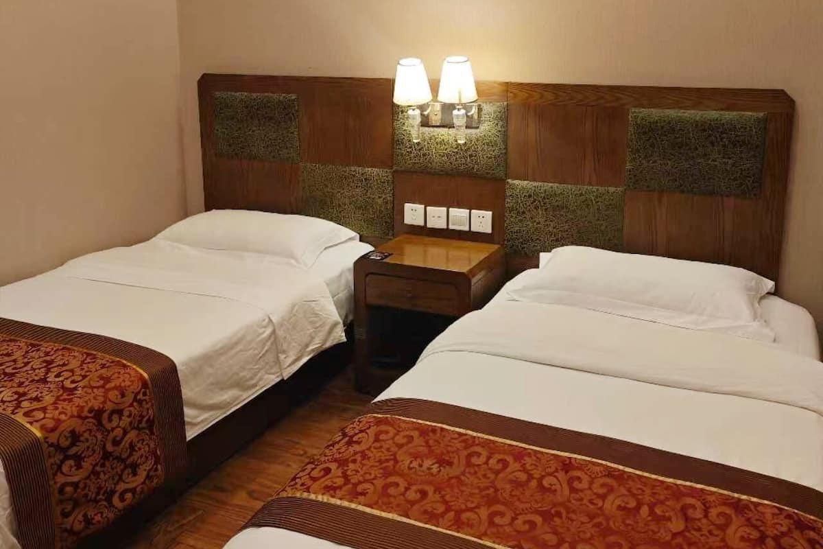 Une chambre d’hôtel avec deux lits simples, une table de chevet avec une lampe et une petite table.