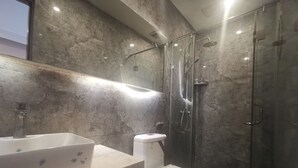 A modern bathroom with a marble wall, a white sink, and a glass-enclosed shower. - Beijing Huiqing Garden Bussiness Hotel (Beijing)