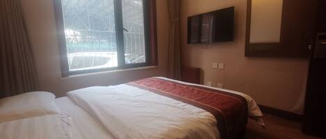 Une chambre d’hôtel avec un grand lit, un téléviseur fixé au mur et une fenêtre donnant sur l’extérieur.