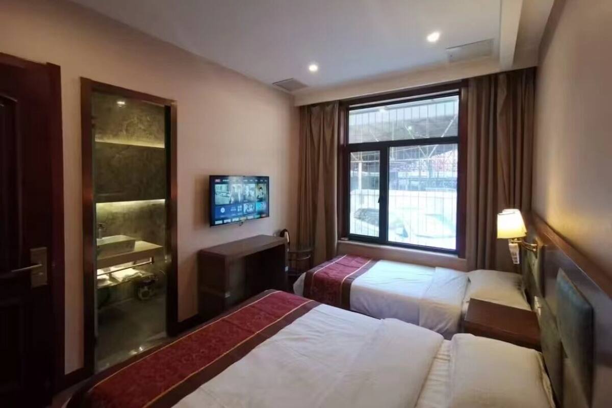 Une chambre d’hôtel avec deux lits, une télévision, une fenêtre avec des rideaux et un espace douche.