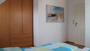 A bedroom with a wooden wardrobe, a bed with a blue and green striped bedspread, and a painting of a beach scene on the wall.