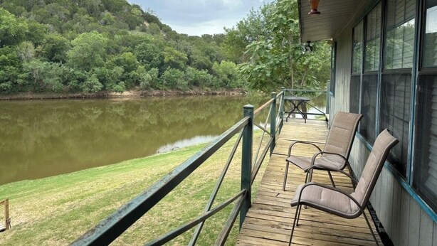 Une terrasse en bois, agrémentée de chaises, qui offre une vue sur un lac, le tout entouré d’une végétation luxuriante et de collines.