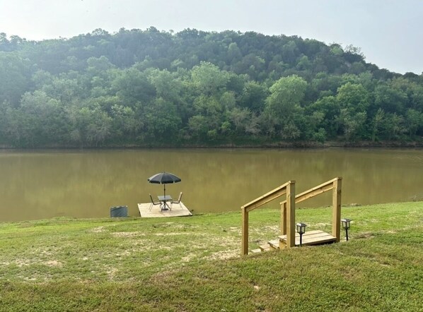 A lakeside area with a wooden deck, a bench, and an umbrella.