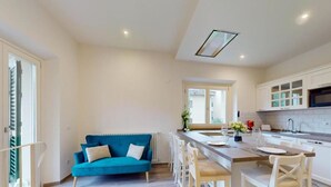 A modern kitchen with white cabinets, a dining area with a blue sofa, and a small island with a sink. - Charming terrace apartment (Firenze)