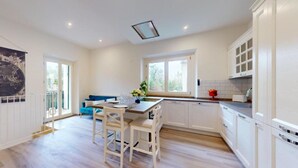 A modern kitchen with white cabinets, a dining area with a blue sofa, and a large window providing natural light. - Charming terrace apartment (Firenze)