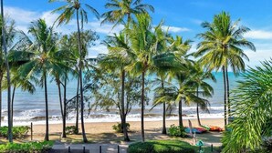 A beach with palm trees, a sandy path, and a view of the ocean.