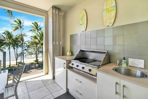 Une cuisine équipée d’une cuisinière à gaz, d’un évier et offrant une vue sur les palmiers et la plage.