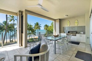 Una cucina moderna con vista sulla spiaggia, un'area pranzo con tavolo in vetro e una ventola a soffitto.