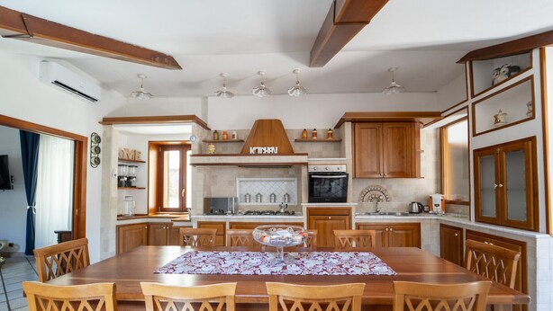 A spacious kitchen with wooden cabinets, a central island, and a dining area with a table and chairs. - Casa Raffaela by Wonderful Italy (Napoli)