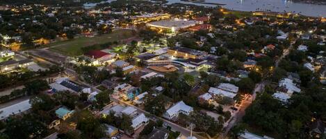 An aerial view of a coastal town with a mix of residential and commercial buildings, a marina with boats, and a large open area that could be a park or sports field.