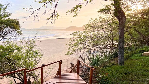 Una escalera de madera que conduce a una playa con vistas al océano y montañas lejanas.