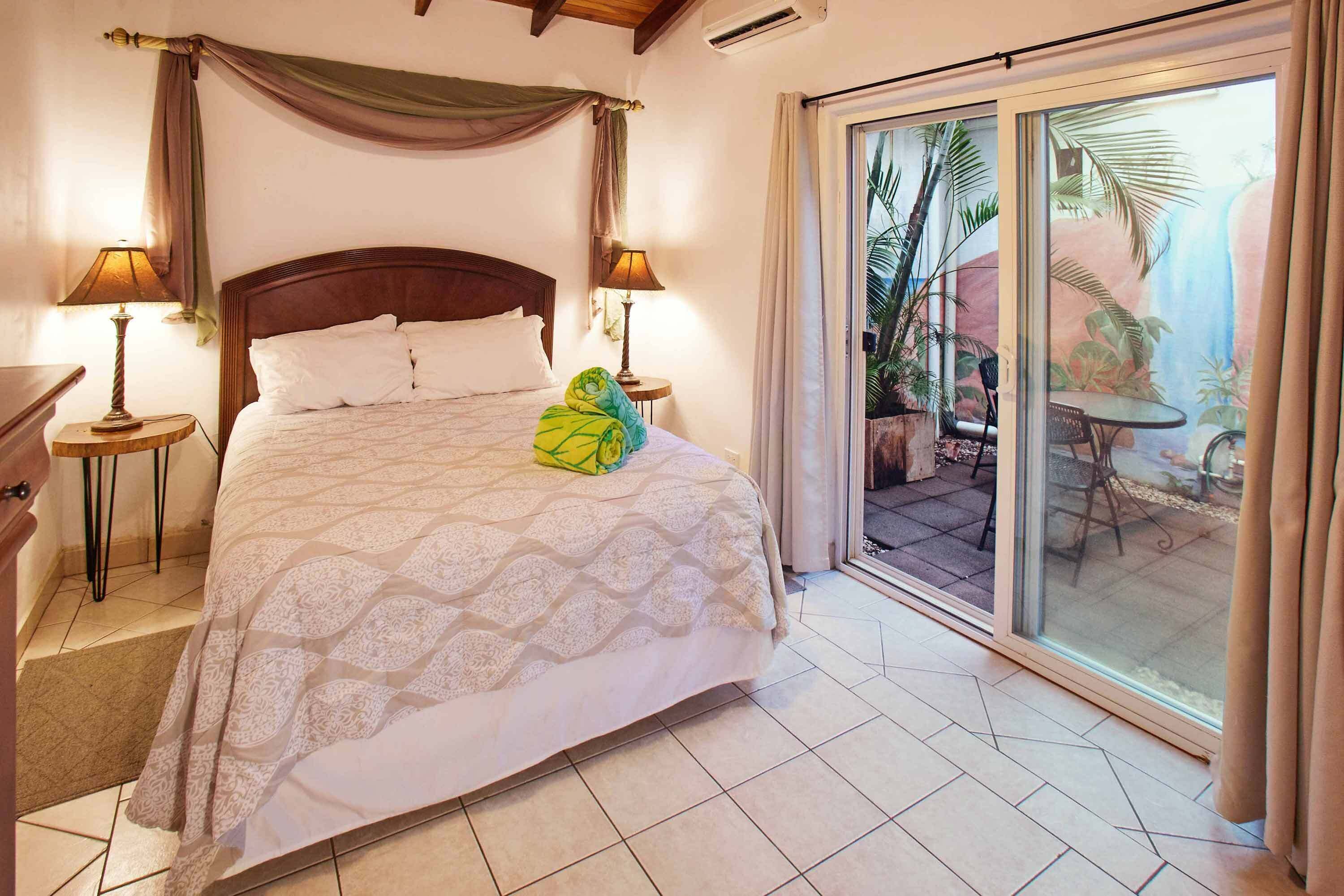 Een slaapkamer met een groot bed, twee bedlampen, een raam met uitzicht op een terras en een schuifdeur met glas.