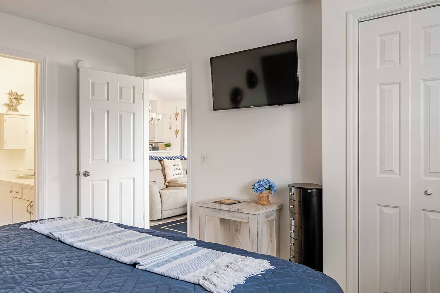 A bedroom with a bed, a TV, a dresser, and a door leading to another room.