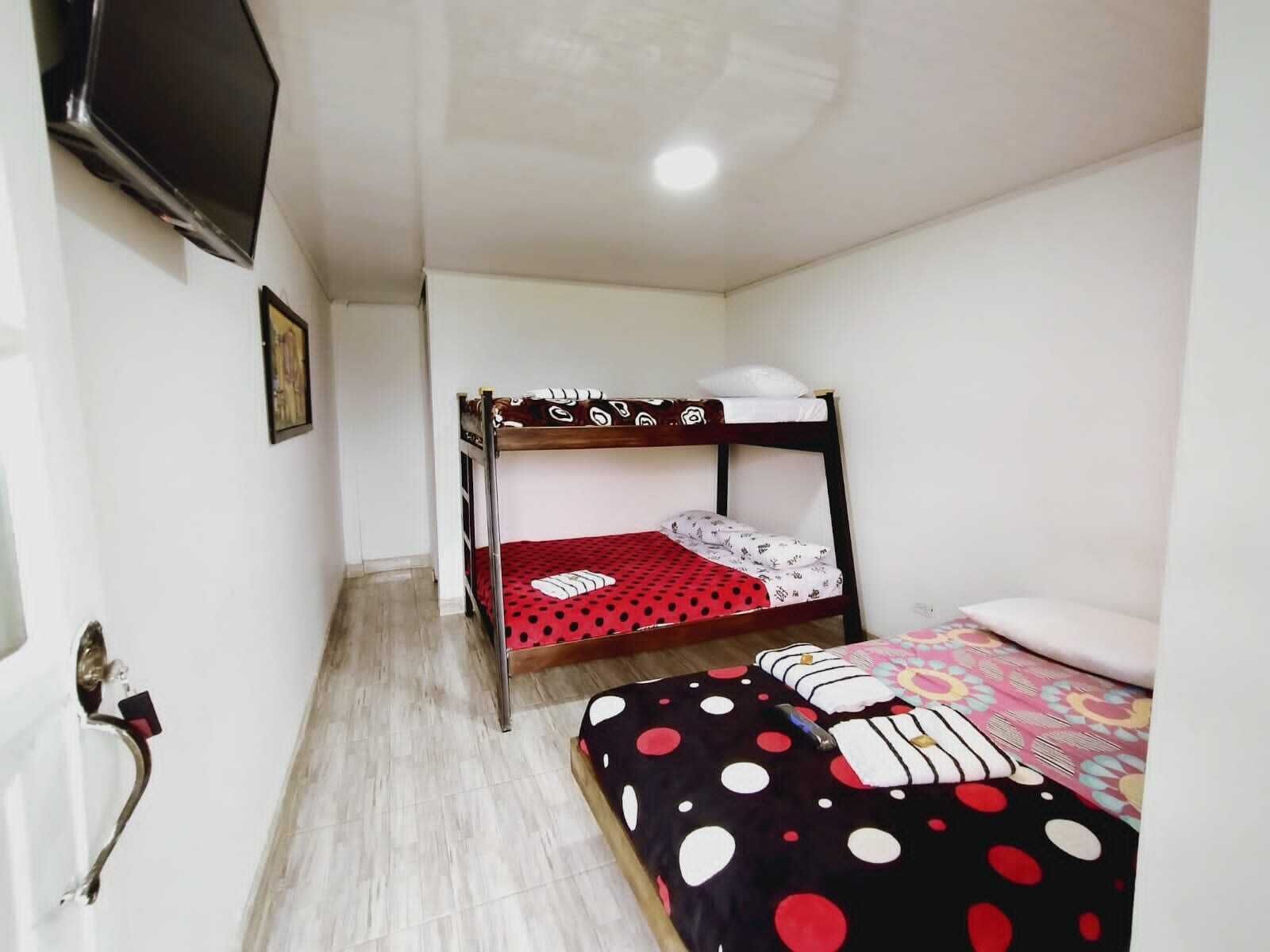 Una habitación pequeña y limpia con una litera, una cama individual, un televisor montado en la pared y un cuadro en el muro.