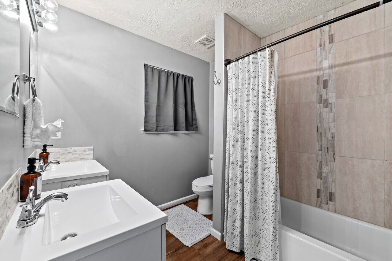 Une salle de bain moderne avec un lavabo blanc, un miroir, un porte-serviettes, des toilettes et un rideau de douche.