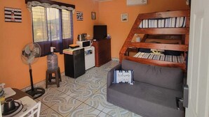 A compact living space with a sofa, a small table, a fan, a water dispenser, and a staircase leading to a loft bed area. - Cozy 1-bedroom guest house with WiFi, AC in fabulous Marcala (La Paz)