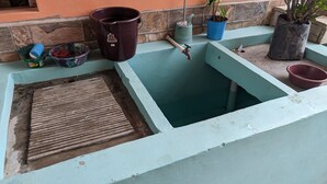 A small, rectangular water tank with a wooden grate, surrounded by potted plants and a trash bin. - Cozy 1-bedroom guest house with WiFi, AC in fabulous Marcala (La Paz)
