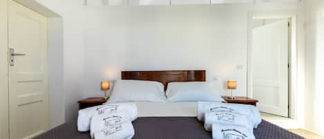 A hotel room with a large bed, two bedside tables with lamps, and a door on the left.