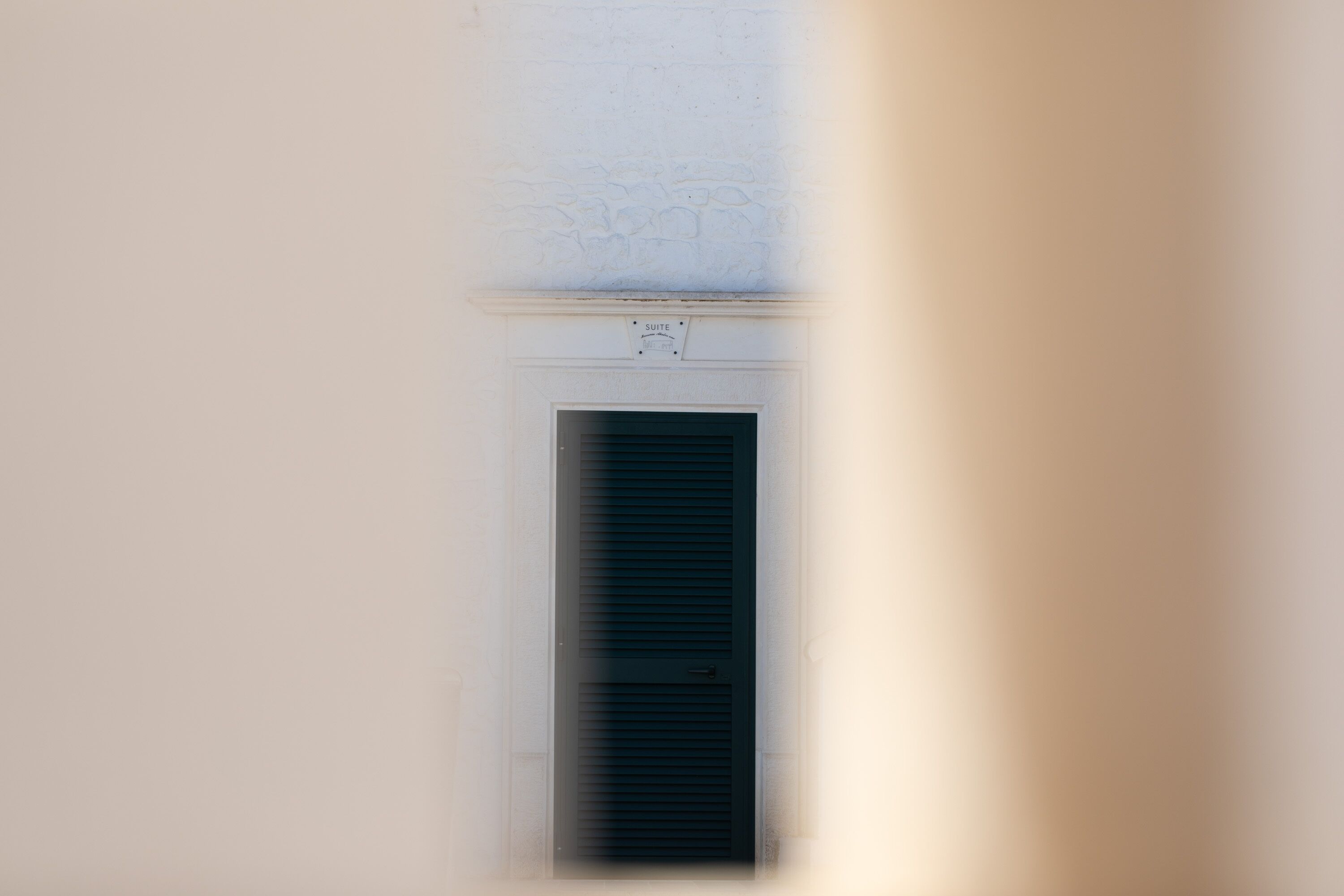 A narrow corridor with a door at the end, a sign above the door indicating a suite, and a textured wall above the door.