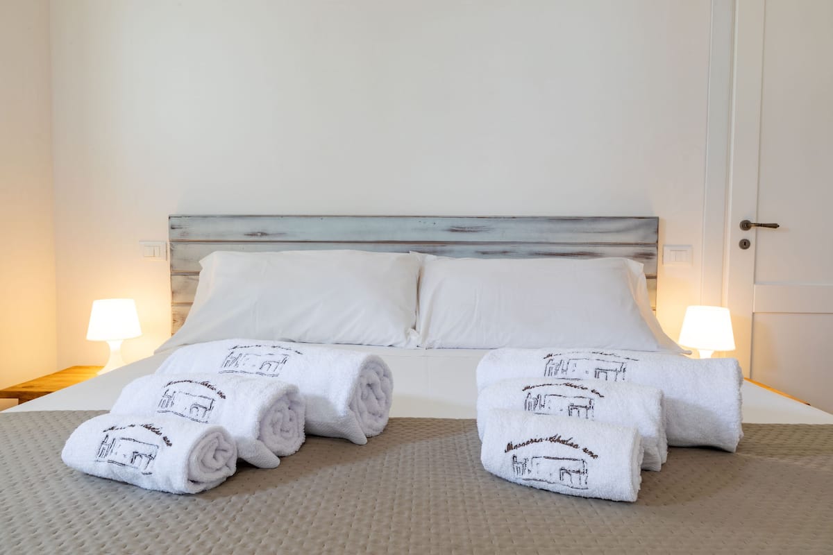 A neatly made bed with white linens and rolled towels featuring a building design, two bedside lamps, and a wooden headboard.