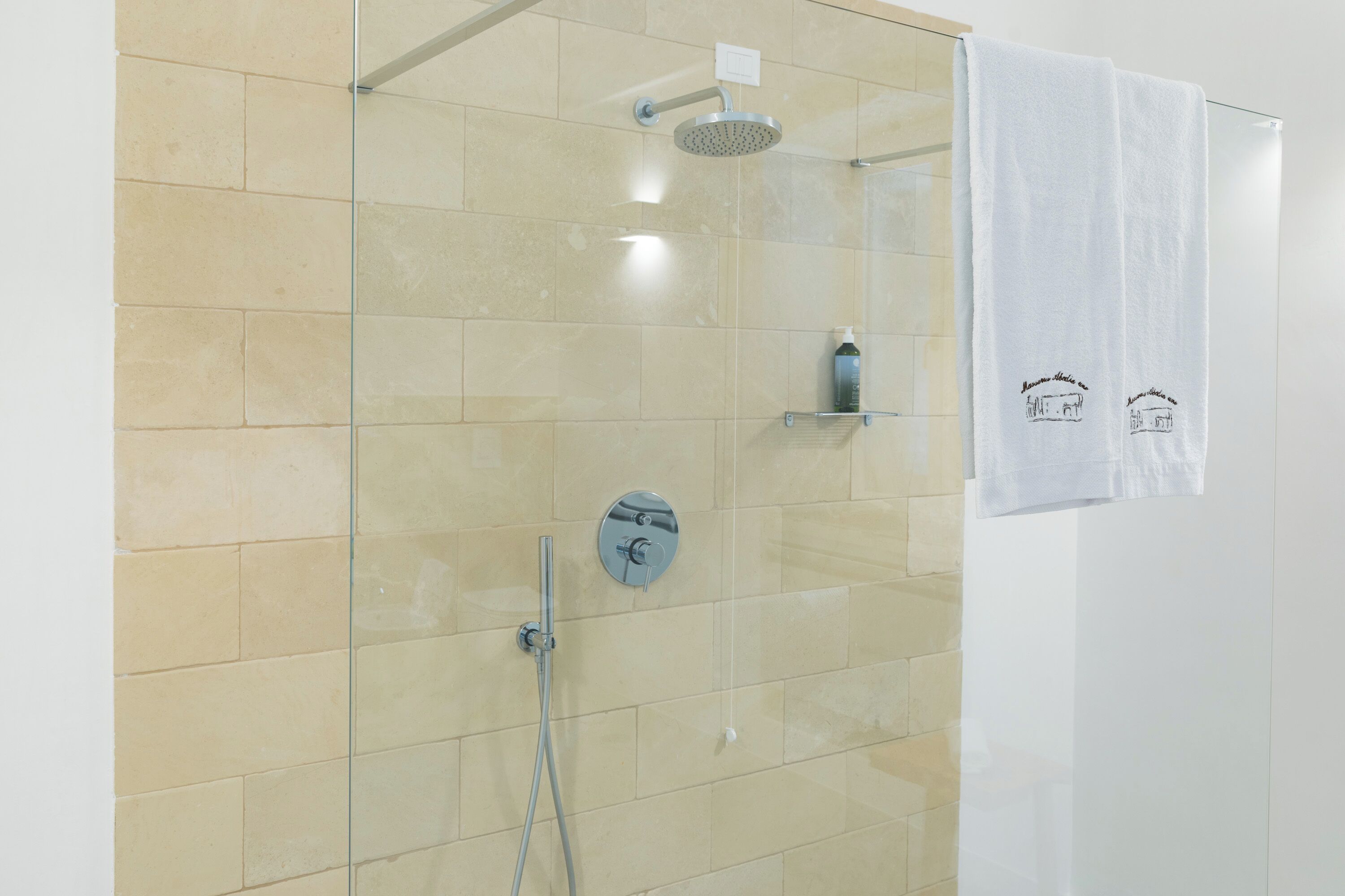 Ducha con cerramiento de vidrio, cabezal de ducha de mano y llave de pared.