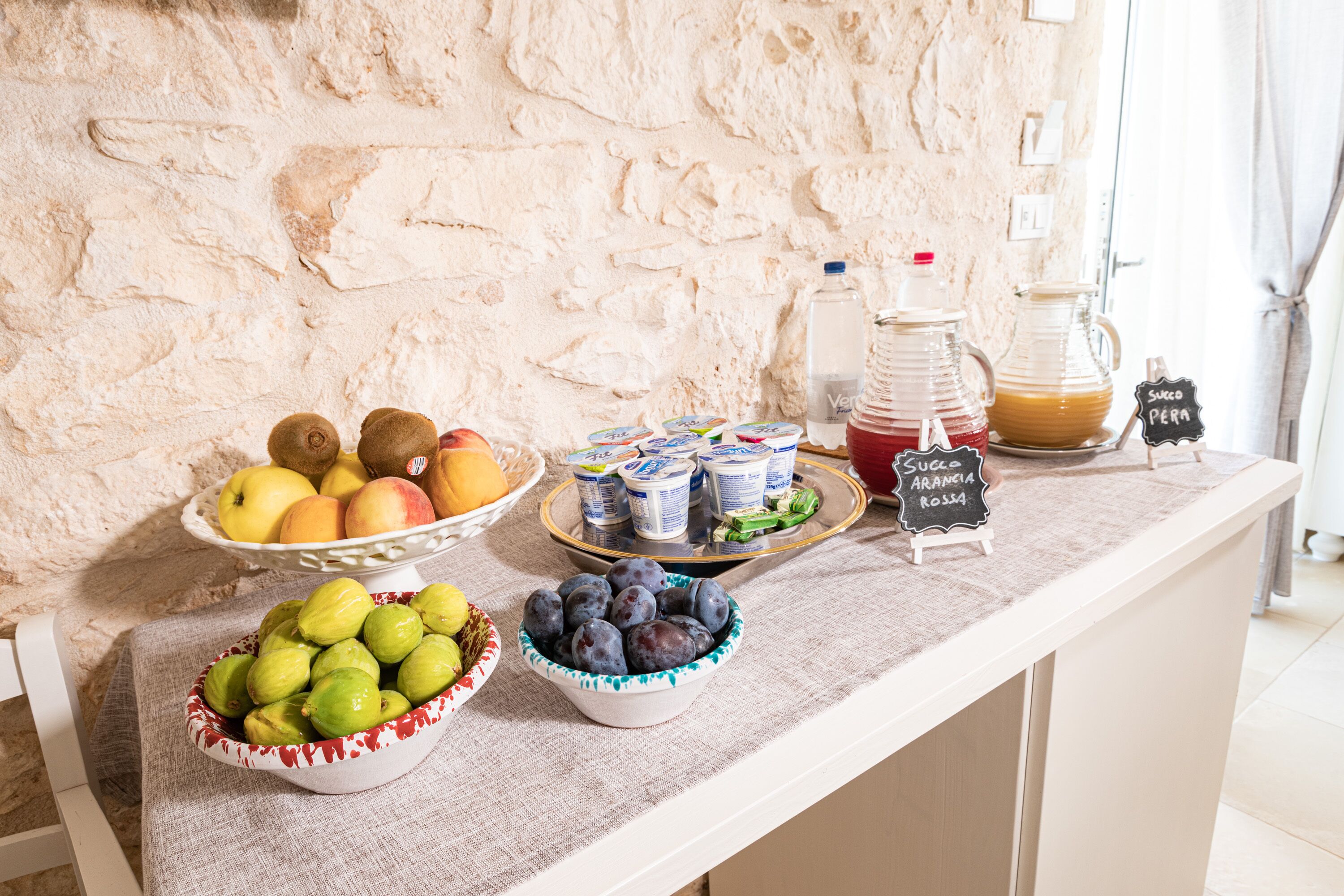 A buffet table with various fruits, yogurt containers, and a pitcher of juice.