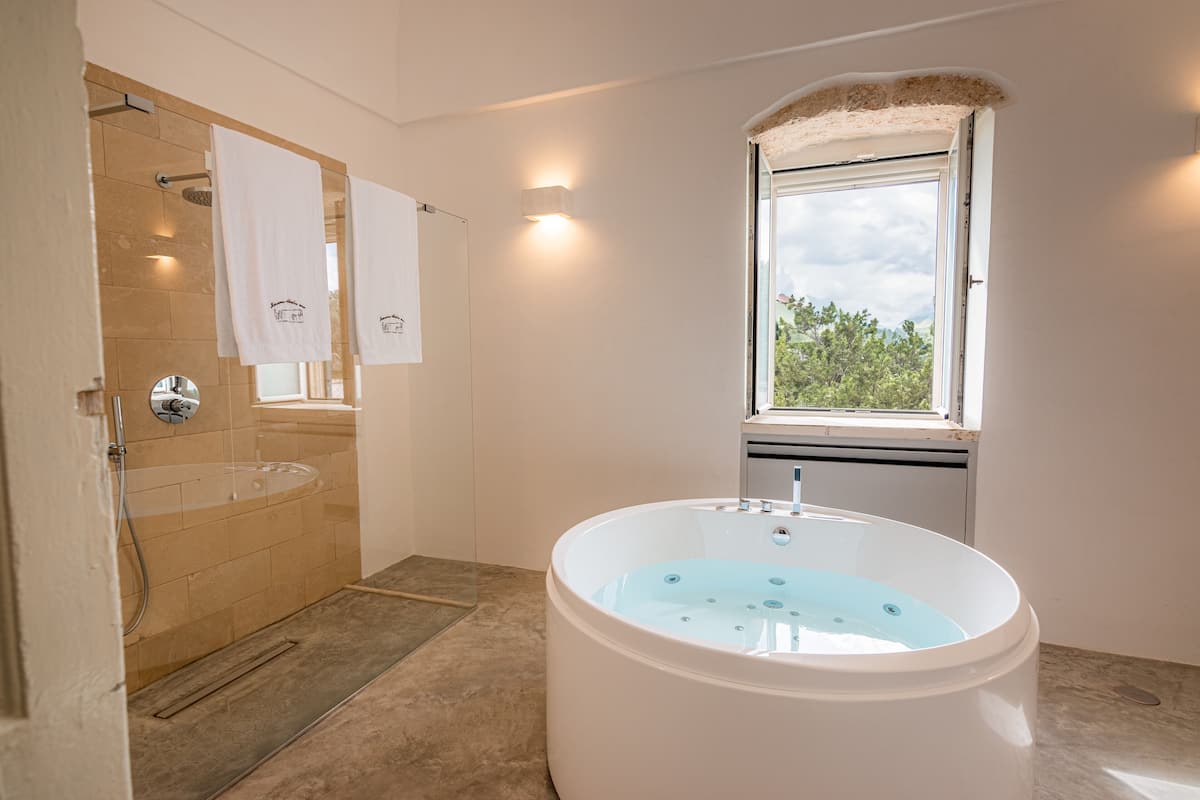 A modern bathroom with a freestanding bathtub, a glass-enclosed shower, and a window providing natural light.