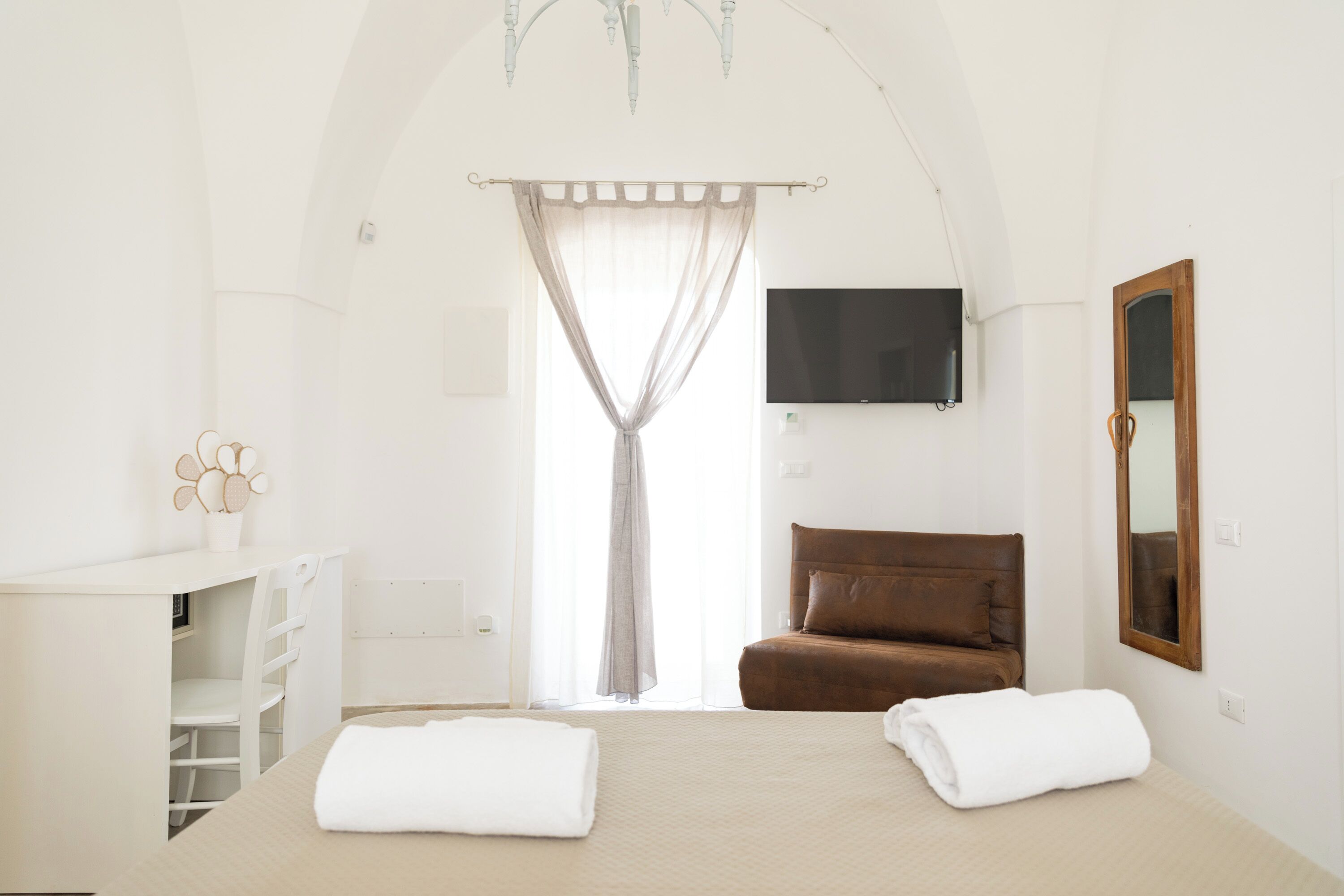 A bedroom with a large bed, a brown sofa, a TV, and a mirror.